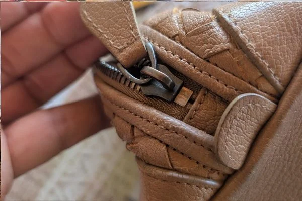 Metal zip with a leather pull tab and woven leather edging, held in a hand