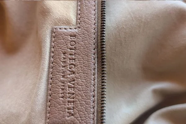 Embossed Bottega Veneta leather tag stitched into the beige lining beside a metal zip