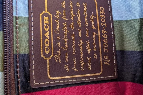 Coach creed patch inside the bag, with style number J0669-10330, against striped lining
