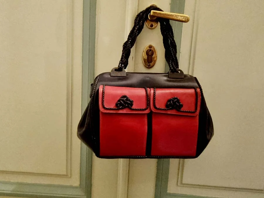 Roberta di Camerino black and red leather bag with two front pockets, hanging by a plaited handle from a door handle