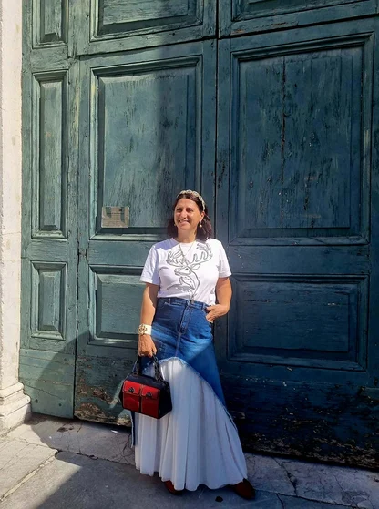 Gracie Opulanza in Lucca in a white T-shirt and denim and tulle maxi skirt, holding a small red and black bag
