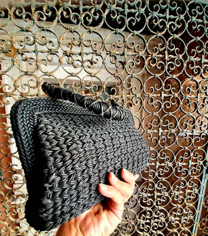 A hand holding the black woven clutch up against an ornate wrought-iron grille