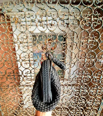 The black woven clutch hanging by its braided handle in front of the wrought-iron grille
