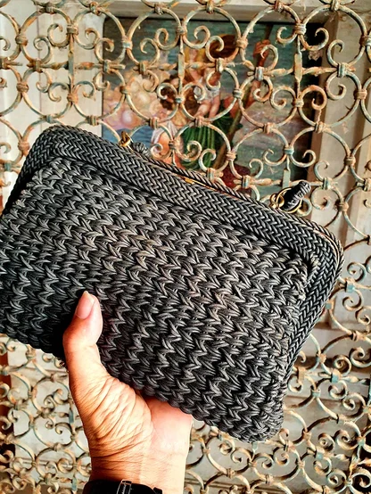 The black woven clutch seen from above in a hand, its tight zigzag weave filling the frame