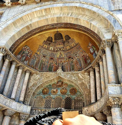 Gold mosaic arch above a marble doorway on the basilica façade in Piazza San Marco, Venice