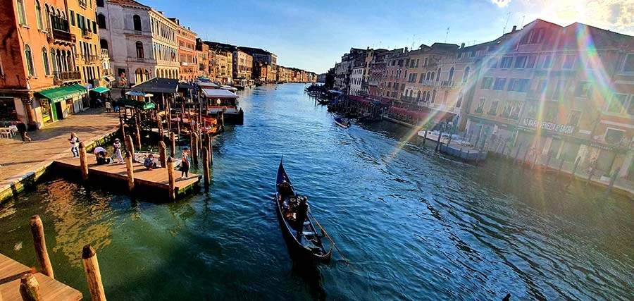 A gondola on the Grand Canal in Venice in low sunlight, with a jetty and palazzi on both banks