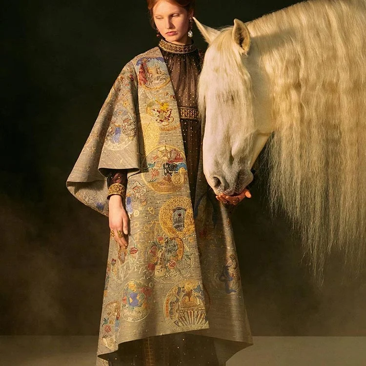 Embroidered Dior haute couture house coat, 2021, worn over a sheer dark dress by a model beside a white horse