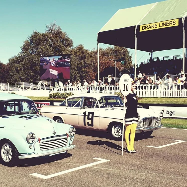 Pale blue and cream vintage saloon cars on the grid, a woman in a black dress and yellow tights holding a number sign