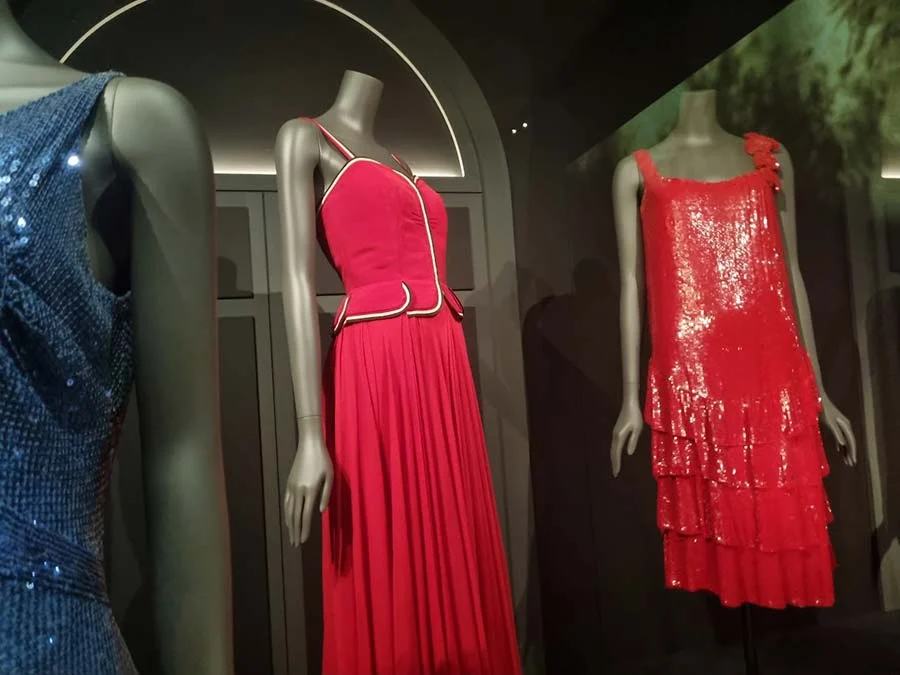 Three dresses at the V&A: blue sequins, a red pleated skirt with white piping, a red tiered sequinned dress